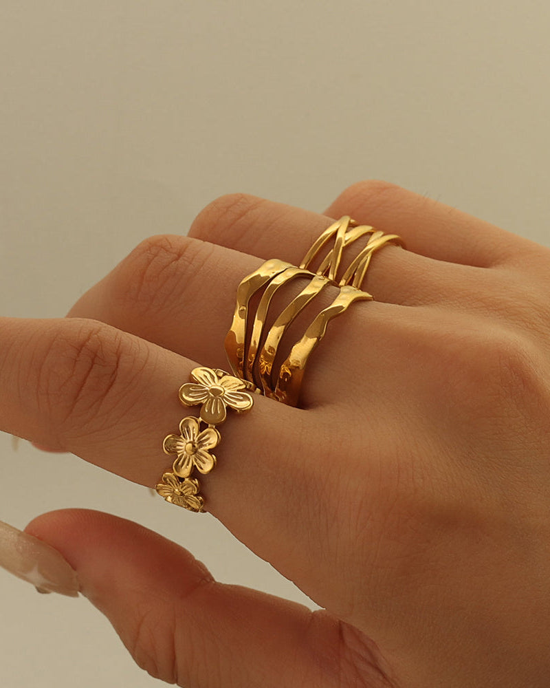 Primer plano de mano con anillo ancho dorado de bandas onduladas y anillo de pequeñas flores.