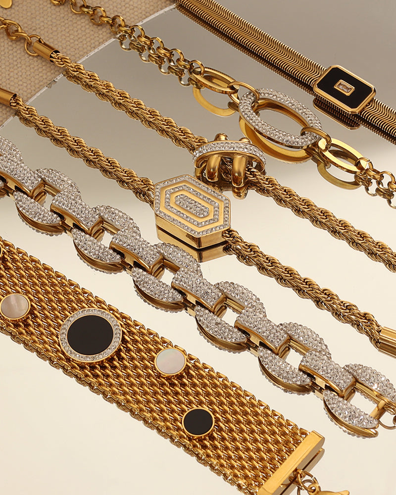 Varias pulseras doradas sobre una superficie reflectante, con diseños de cadenas, lazos y círculos negros.