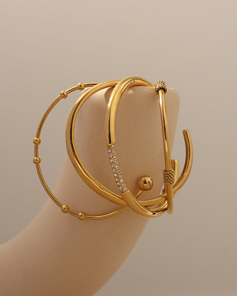 Varias pulseras rígidas doradas, con esferas y detalles brillantes, alrededor de un soporte curvo claro.