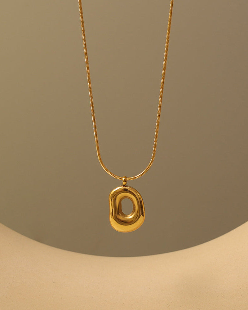 Collar dorado con colgante ovalado irregular de centro hundido y brillante, suspendido sobre fondo beige.