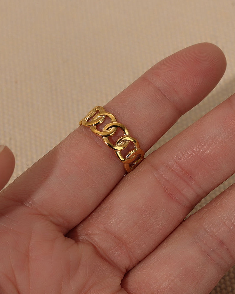Primer plano de anillo dorado de eslabones anchos entrelazados, puesto en un dedo.