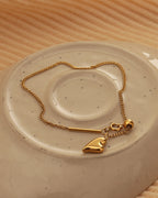 Collar fino dorado con pequeño corazón liso colgante, dispuesto en círculo sobre plato de cerámica claro.
