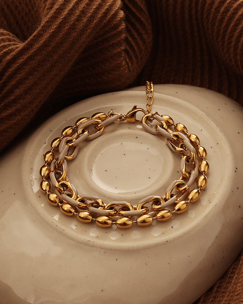 Pulsera de dos cadenas doradas con eslabones ovalados y detalles oscuros, sobre un plato de cerámica.