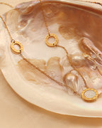 Collar fino dorado con tres motivos redondos de centro blanco nacarado, extendido sobre una concha.