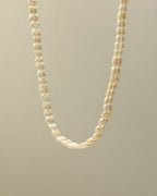 Collar de pequeñas perlas blancas irregulares suspendido sobre fondo beige.
