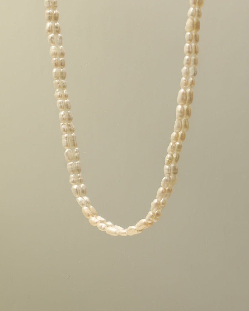 Collar de pequeñas perlas blancas irregulares suspendido sobre fondo beige.