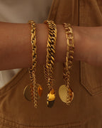 Tres pulseras doradas de cadenas de distintos eslabones con discos redondos colgantes, puestas en la muñeca.