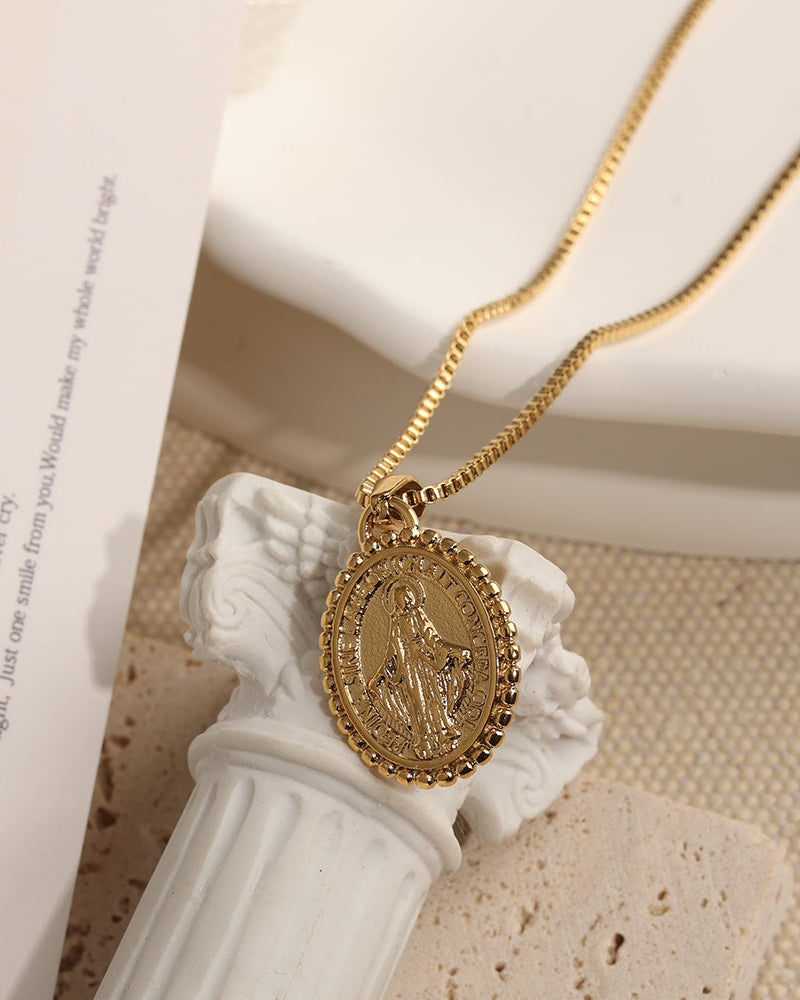 Collar dorado con medallón ovalado de figura en relieve y borde decorado, sobre una pequeña columna blanca.