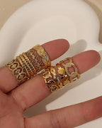 Varios anillos dorados de eslabones y bandas decoradas, sostenidos sobre los dedos de una mano.