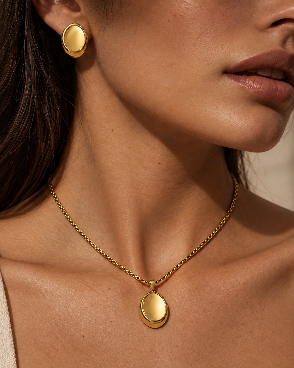 Mujer con collar dorado de colgante ovalado liso y brillante y pendiente ovalado a juego.