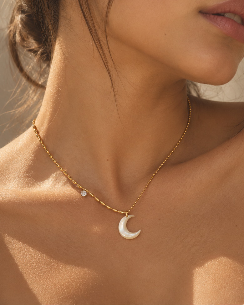 Mujer con collar fino dorado y colgante blanco nacarado de media luna, con una pequeña cuenta clara en la cadena.