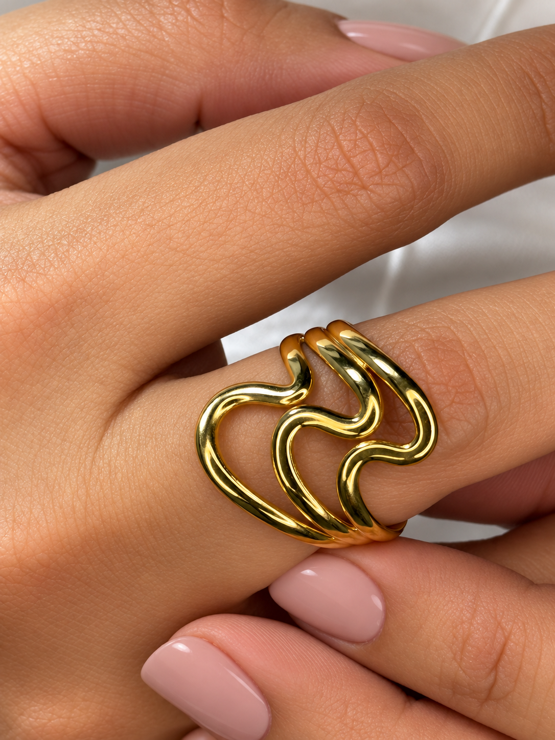 Primer plano de un anillo dorado de ondas abiertas de Xihe By Dm, sobre la mano de una modelo con uñas nude.