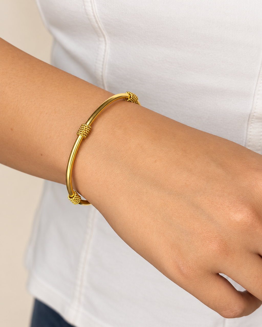 Brazalete rígido dorado de Xihe By Dm con tres detalles trenzados visibles, en la muñeca de una modelo sobre una blusa blanca.