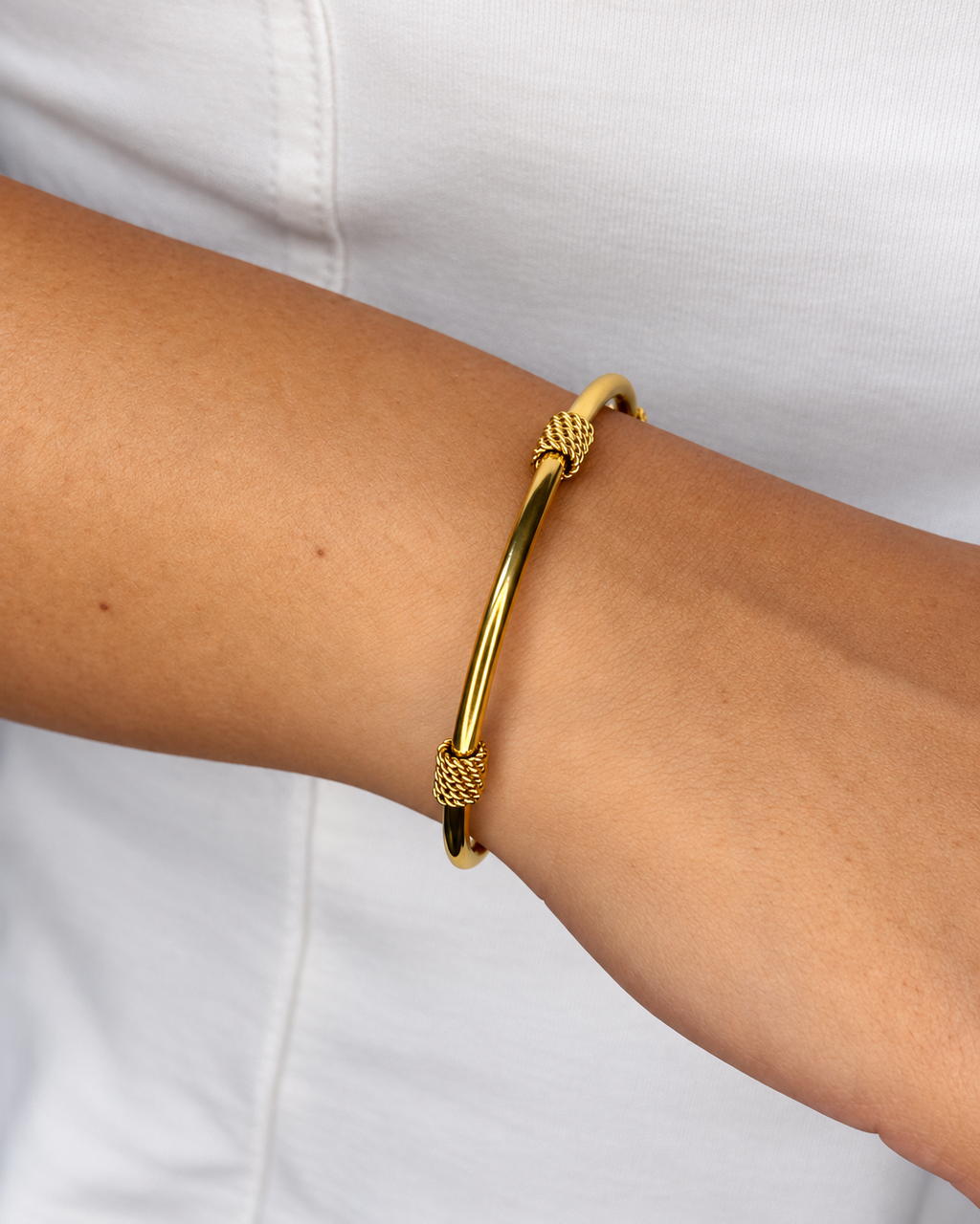 Brazalete rígido dorado de Xihe By Dm con dos detalles trenzados, en la muñeca de una modelo sobre una blusa blanca.