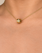 Primer plano de un collar dorado de Xihe By Dm con colgante cilíndrico pulido y detalles de corazones brillantes.