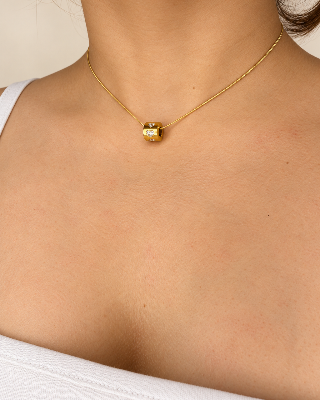 Collar de cadena fina dorada de Xihe By Dm con colgante cilíndrico decorado con corazones brillantes, sobre el escote de una modelo.
