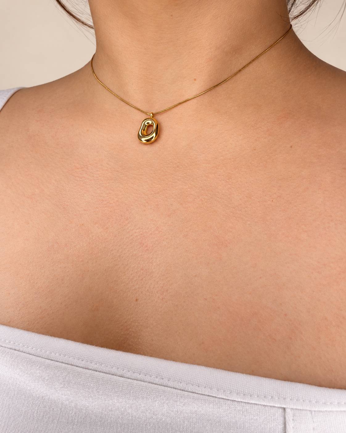 Collar de cadena fina dorada de Xihe By Dm con colgante ovalado irregular, centro abierto y acabado pulido, sobre el escote de una modelo.