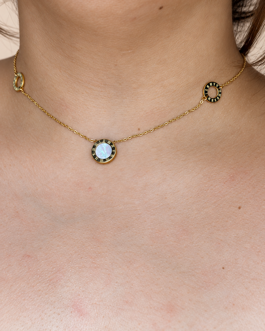 Collar dorado de Xihe By Dm con detalle central nacarado y aros de números romanos, sobre el escote de una modelo.