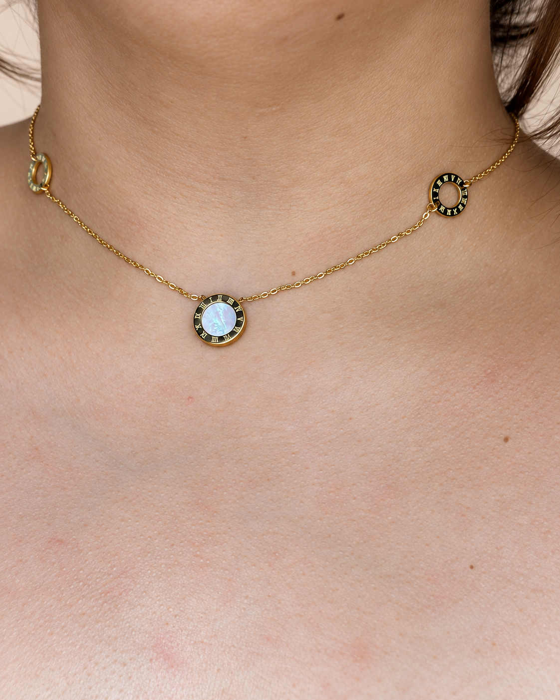 Collar dorado de Xihe By Dm con detalle central nacarado y aros de números romanos, sobre el escote de una modelo.