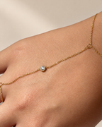 Detalle de la pulsera anillo de Xihe By Dm, con cadena fina dorada y piedra redonda brillante sobre el dorso de la mano.