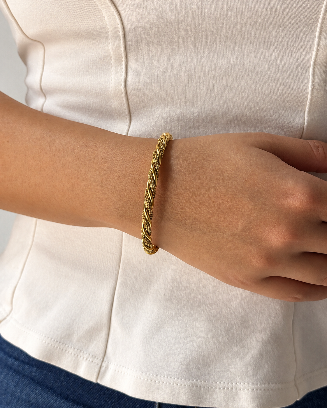 Pulsera dorada de diseño trenzado de Xihe By Dm en la muñeca de una modelo sobre una blusa blanca.