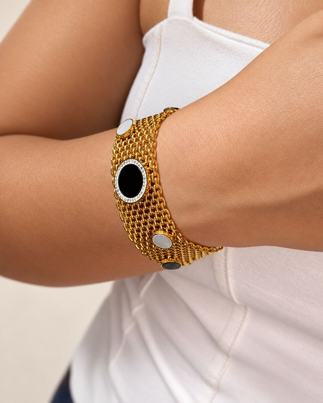 Pulsera de malla dorada de Xihe By Dm con centro negro rodeado de piedras brillantes y detalles nacarados, en la muñeca de una modelo.